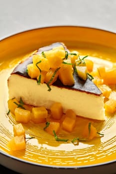 Luxurious slice of cheesecake topped with caramelized mango cubes and fresh mint shavings, creating perfect balance of creamy and fruity flavors, served on yellow plate