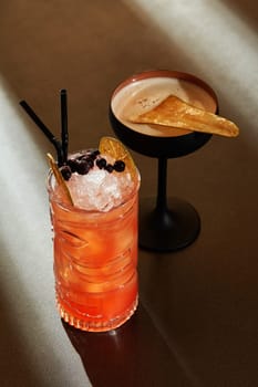 Striking pair of cocktails, vibrant Zombie cocktail crowned with berries, and spiced pear drink with caramelized garnish, awaiting in elegant glasses on bar