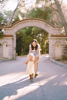 Mom walks along the road with her arms open for a little running laughing girl. High quality photo