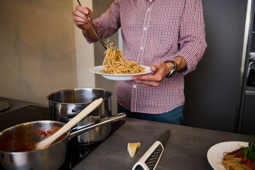 Close-up male chef plating up dish with freshly boiled spaghetti before serving it, cooking family dinner at home kitchen. People. Culinary. Lifestyle