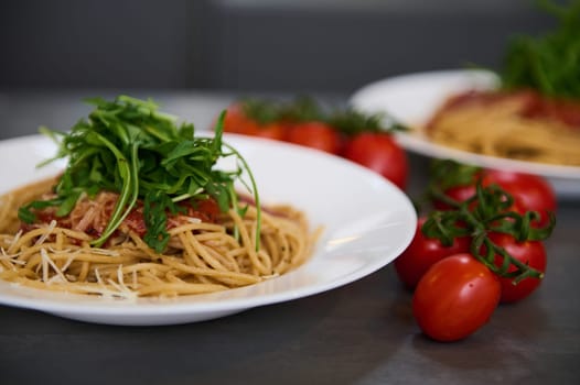 Italian spaghetti capellini with tomato sauce, parmesan cheese and arugula leaves. A branch of fresh ripe organic tomato cherry on the kitchen table.