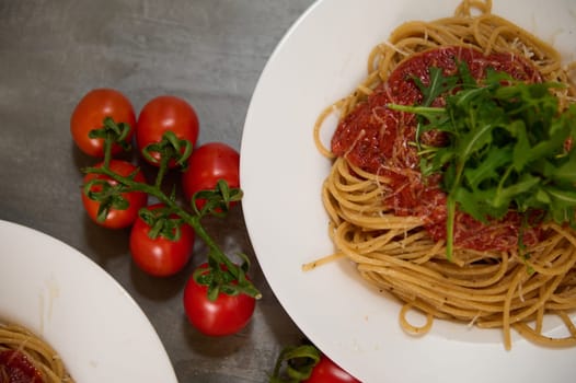 Food background with a branch of fresh ripe organic tomatoes cherry near plates of Italian pasta spaghetti a la Amatriciana with pancetta bacon and pecorino parmesan cheese. Italian cuisine. Top view