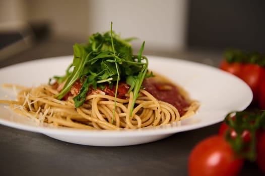 Food background with a branch of fresh ripe organic tomatoes cherry near plates of Italian pasta spaghetti a la Amatriciana with pancetta bacon and pecorino parmesan cheese. Italian culinary