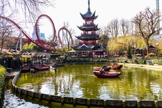 Tivoli amusement park with Japanese tower pond and boats with people in Copenhagen, Denmark - April 28, 2024
