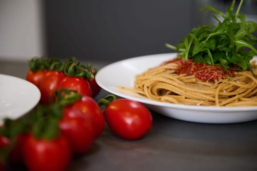 Yummy pasta capellini with tomato sauce and basil green arugula leaves on white plates near a bunch or red cherry tomato. Food background. Italian cuisine, culture and traditions. Epicure. Gastronomy