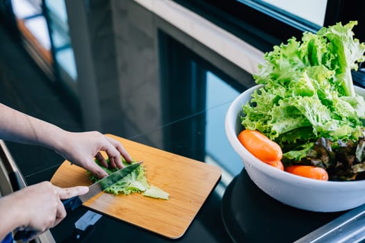 An unrecognizable woman in a blue apron prepares a healthy dinner cutting fresh vegetables for a nutritious salad. Close-up view of the housewife making a delicious meal in her kitchen.