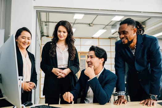 In a collaborative meeting, coworkers gather around a desktop computer, actively discussing strategy and brainstorming ideas. Their diverse backgrounds contribute to successful teamwork and planning.