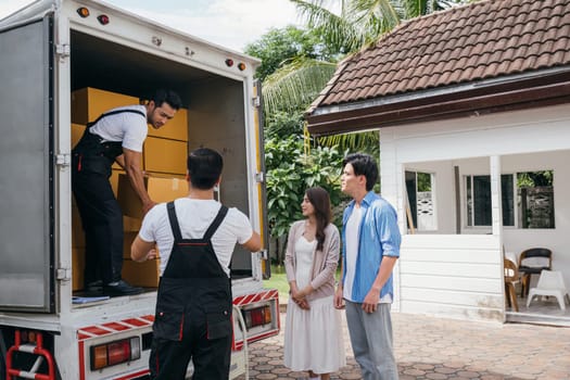 Team of workers assists a couple in moving into their new home. Together they unload and lift cardboard boxes showcasing professional and efficient delivery service. Moving Day Concept