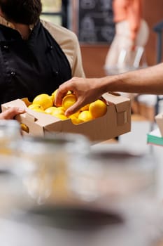 Close-up of the merchant holding crates of locally grown lemons while customer chooses one. Detailed image of male vendor carrying a box of freshly harvested organic produce.