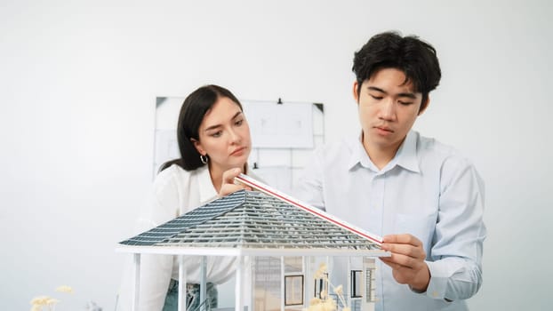 Professional young beautiful architect engineer using ruler and pencil measuring model roof length at modern office with blueprint hanged behind. Creative design and teamwork concept. Immaculate.