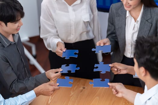 Corporate officer worker collaborate in office, connecting puzzle pieces with report paper on table as partnership and teamwork. Unity and synergy in business concept by merging jigsaw puzzle. Concord