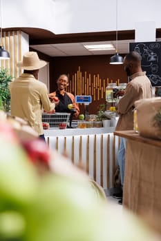 African American business owner assists a male customer at a bio supermarket counter with eco friendly, zero-waste options. Local and organic products are highlighted. Focus on background.