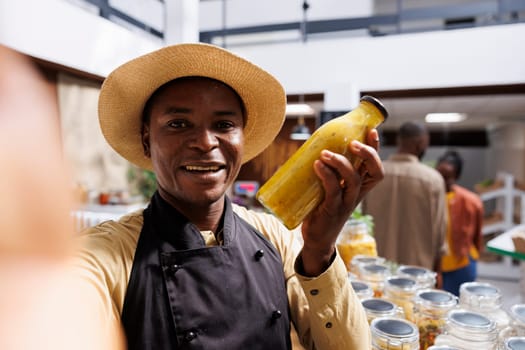 African American business owner promotes fresh, organic products. Filming with smartphone, he showcases eco friendly packaging and glass jars with healthy food. Ideal for advertising.