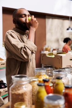 Image shows an African American male client inhaling the freshness of a green apple at local store. Detailed shot of a black man holding and admiring the locally grown fruit in the eco friendly shop.