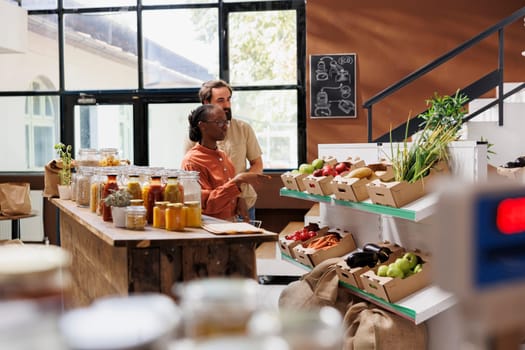 Portrait of caucasian boyfriend and african american girlfriend using shopping basket to purchase fresh fruits and vegetables. Smiling multiracial clients in local grocery shop buying organic produce.