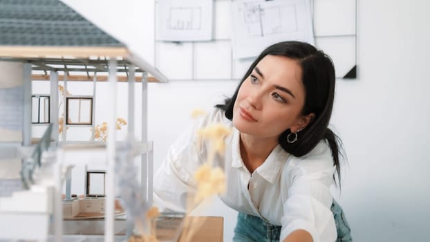 Young beautiful caucasian architect engineer turns house model around to inspect house construction and check mistake point to solve the problem on meeting table at modern office. Closeup. Immaculate.