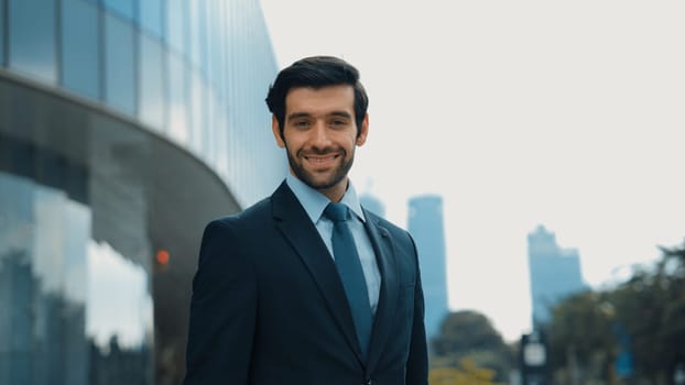 Professional businessman standing at city or park. Smiling project manager looking at camera while smiling arms with confident. Closeup of investor wearing suit at architectural building. Exultant.