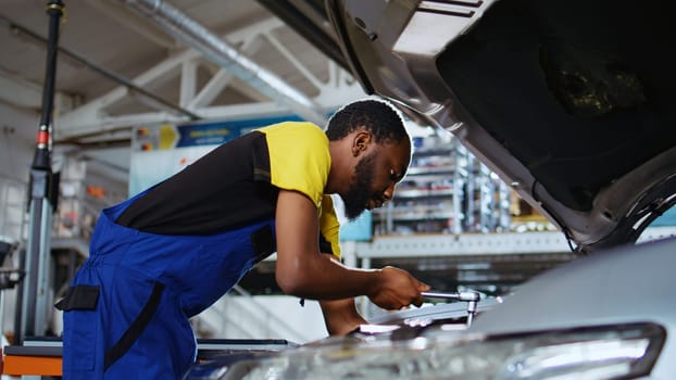 Meticulous specialist in car service picks torque wrench from work station bench, using it to tighten screws after replacing engine. Professional in garage fixing client automobile, close up shot