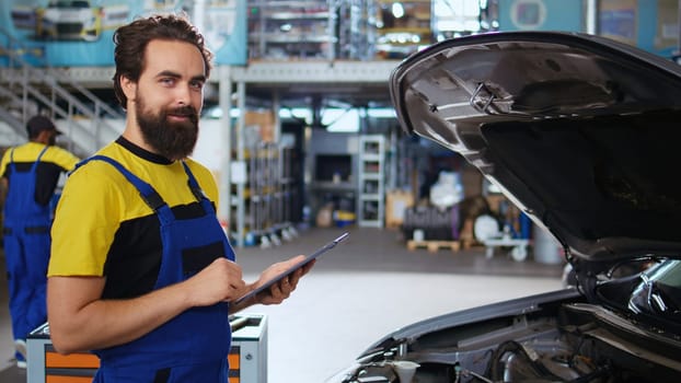 Dolly in shot of serviceman assisting customer with car maintenance in repair shop. Employee in garage workspace looking over automobile parts with woman, repairing her vehicle during routine checkup