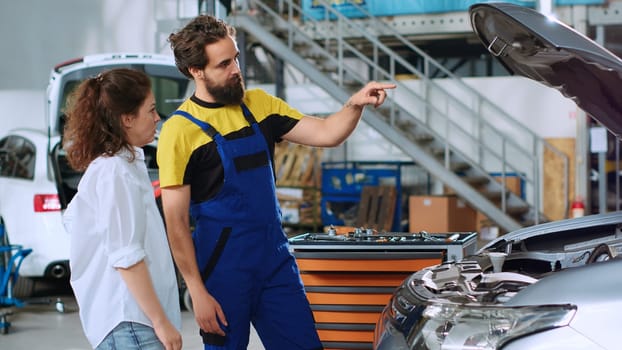 Mechanic in car service using augmented technology hologram to show woman automobile reaction to road conditions after fixing it. Repairman using AR technology with client to test vehicle engine