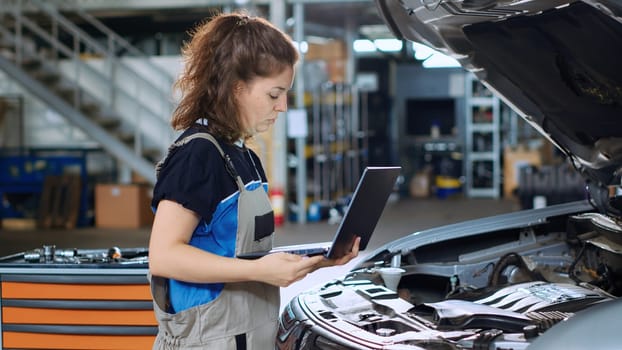 Engineer in garage workspace using laptop to order new parts for car after finding damages during annual checkup. Auto repair shop specialist looking online for vehicle components