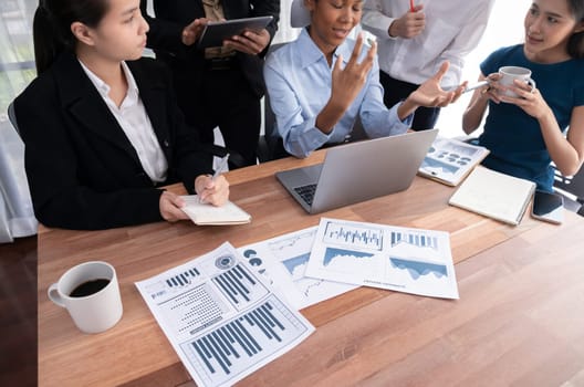 Multiracial analyst team use BI dashboard data to analyze financial report on meeting table. Group of diverse business people utilize data analysis by FIntech for success business marketing. Concord