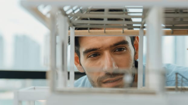 Closeup of young caucasian skilled architect engineer focusing on checking the house model structure with confident. Male worker looking at house construction. Creative design concept. Tracery