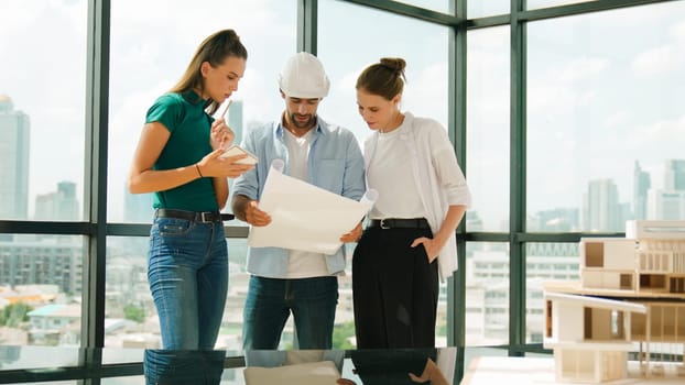 Professional architect engineer team talking, sharing, brainstorming about design while manager hold at project plan. Young architect holding plan while manager listen and point at plan. Tracery