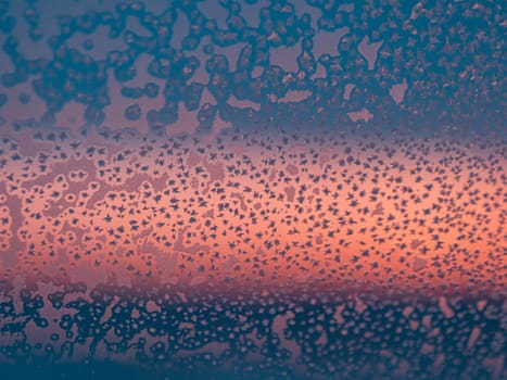 Frozen window with frost patterns overlooking colorful sunset in winter evening