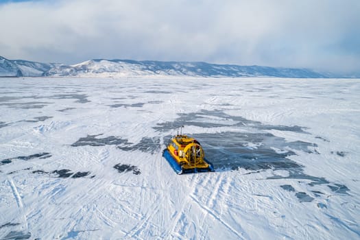 Aerial view on a hovercraft parked on the beautiful cracked ice of the lake Baikal. Winter Baikal, frozen lake. Amazing winter landscape.