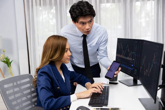 Smiling businessman showing dynamic stock market data on mobile phone to woman writing to memo for analyzing profit value currency rate online website program application at home office. Infobahn.