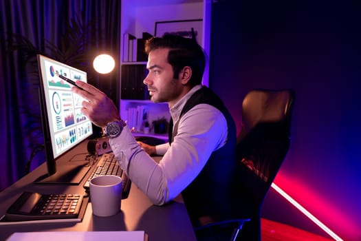 Smart businessman pointing with pen on desk to focusing research target market in service product database online channel on pc screen at purple neon dark light home office at night time. Surmise.