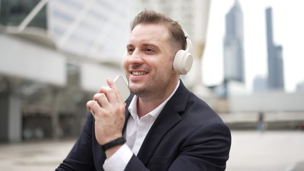 Professional business man listening headphone and using phone record voice while sitting at stair in urban city. Manager using headset listening relaxed song and moving along in lively mood. Urbane.