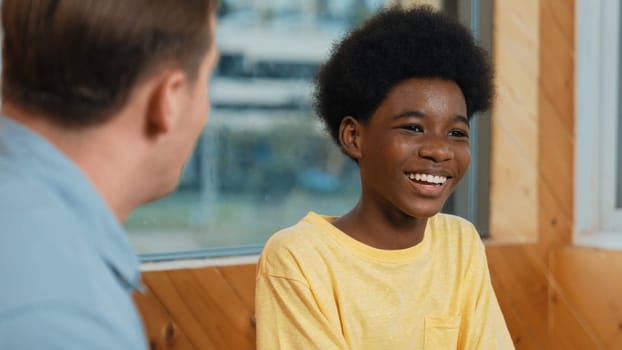 Smiling african boy sitting in circle while listening diverse friend sharing idea in group therapy with trust. Highschool student thinking and learning about mental health problem. Edification.