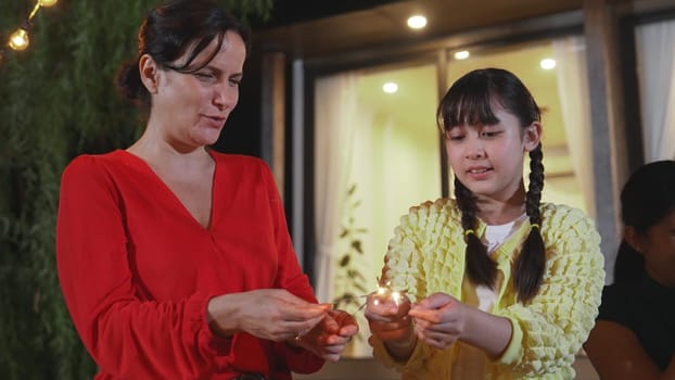 Happy family hold glowed sparkler in holiday celebration party. Daughter, mother and grandmother enjoy play spark together. Outdoor activity to cross generation gap strengthen family bond. Divergence.