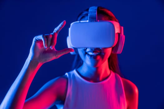 Female standing surrounded by neon light wear VR headset connecting metaverse, futuristic cyberspace community technology, spreading index and thumb finger interacting virtual object. Hallucination.