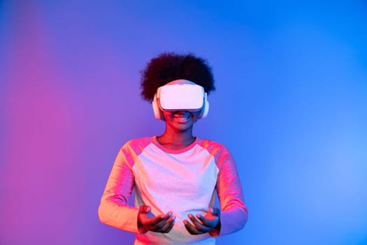 Young African wearing VR glasses through metaverse holding data learning application on blue pink neon lighting gradient technology digital innovation 3D studying hologram graphic assist. Contrivance.