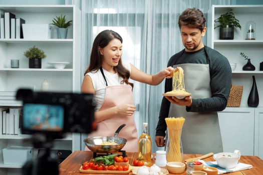 Couple chef influencers cooking special homemade of spaghetti with tongs taking to frying pan, putting seasoning and tasty sauce to make good flavor, recording on camera with live chanel. Postulate.