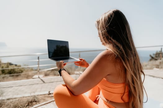 Digital nomad, Business woman working on laptop by the sea. Pretty lady typing on computer by the sea at sunset, makes a business transaction online from a distance. Freelance, remote work on vacation