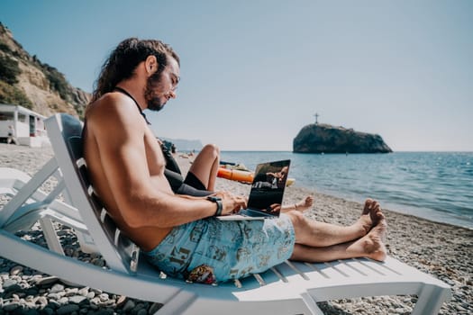 Digital nomad, Business man working on laptop by the sea. Man typing on computer by the sea at sunset, makes a business transaction online from a distance. Freelance, remote work on vacation