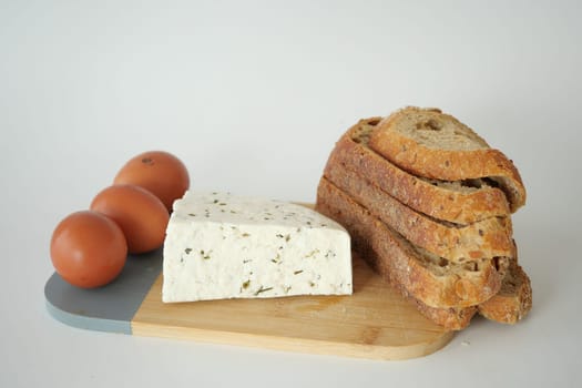 cheese slice, eggs and stack of breads on a chopping board on white background .