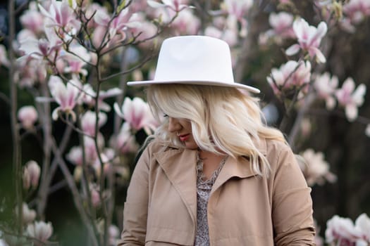 Magnolia flowers woman. A blonde woman wearing a white hat stands in front of a tree with pink flowers