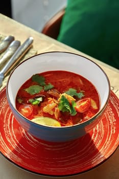 Hot and spicy Thai soup tom yum with shrimps, squid, shiitake mushrooms and cherry tomatoes garnished with fresh parsley and lime wedge traditionally served in chawan. Authentic Asian cuisine