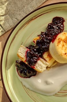 Homemade sweet syrniki topped with creamy cheese cream and rich berry jam, served on rustic ceramic plate