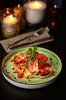 Savory bruschetta topped with tender veal steak, crispy bacon strips, spicy piquant sauce and fried onions, garnished with fresh cherry tomatoes and greens, on ceramic plate in intimate dining setting