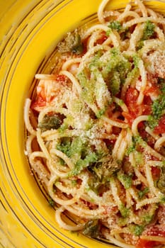 Closeup of colorful rich Italian style Arrabbiata Pasta with shrimp and crispy caper chips, seasoned with fragrant spicy tomato, chili and garlic sauce, sprinkled with grated parmesan, on yellow plate