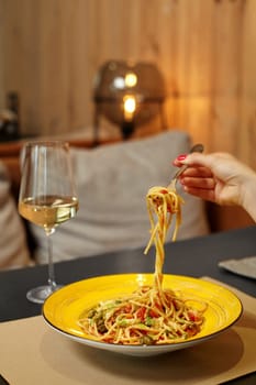 Woman twirling spaghetti with rich blend of pesto, tomato sauce and parmesan on fork enjoying Arrabbiata Pasta with shrimp and capers, accompanied with white Italian wine. Gastronomic pleasure concept