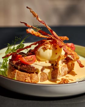 Close-up of savory Mediterranean-style bruschetta with slices of veal steak, crispy bacon strips, poached egg, spicy piquant sauce and fried onions, garnished with fresh cherry tomatoes and greens