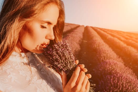 Close up portrait of young beautiful woman in a white dress and a hat is walking in the lavender field and smelling lavender bouquet.