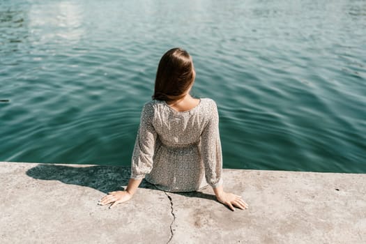A woman is sitting in the water wearing a dress. The water is calm and clear. The woman is enjoying the moment and taking in the beauty of the water